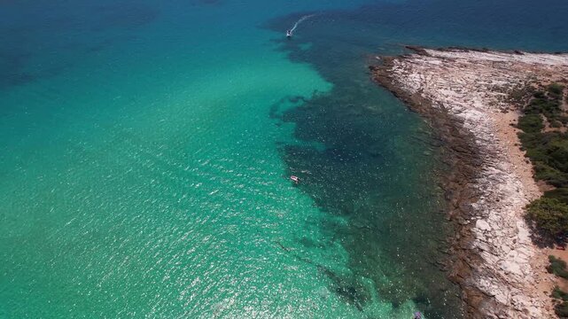 Beautiful aerial view of a sandy beach with crystal clear sea, turquoise water and visitors enjoying swimming and paddleboarding on Thassos Island, Greece.
