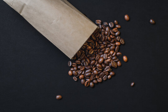 Diagonal view of roasted coffee beans spilling from craft bag on dark background