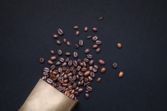 Creative flat lay composition with coffee grains scattering from paper packaging in the corner of dark frame.
