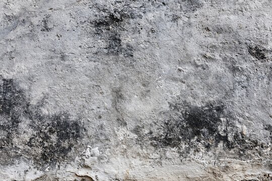 The weathered concrete wall with aged texture, gritty surface, and dark patches