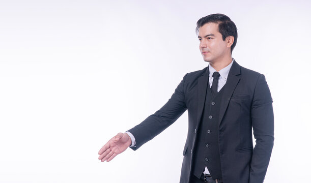 Confident handsome businessman in dark suit extending hand aside for handshake or presenting on white background with copy space. Professional executive welcoming partner for business deal.