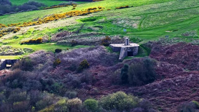 Aerial view of a concrete bunker nestled in a hilly landscape with purple and green vegetation in France.