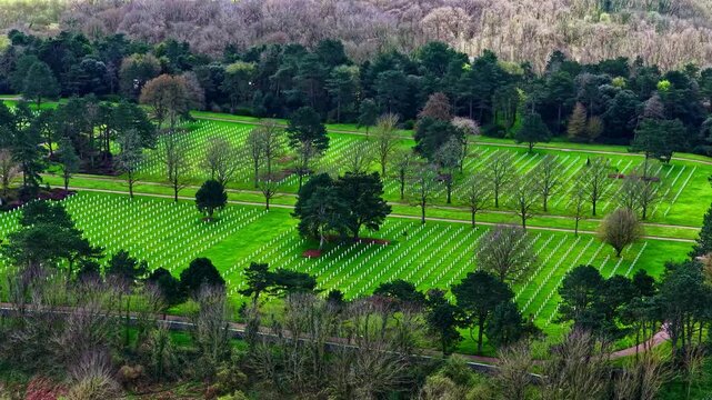 Aerial view of rows of white crosses in a military cemetery surrounded by lush green trees in France.