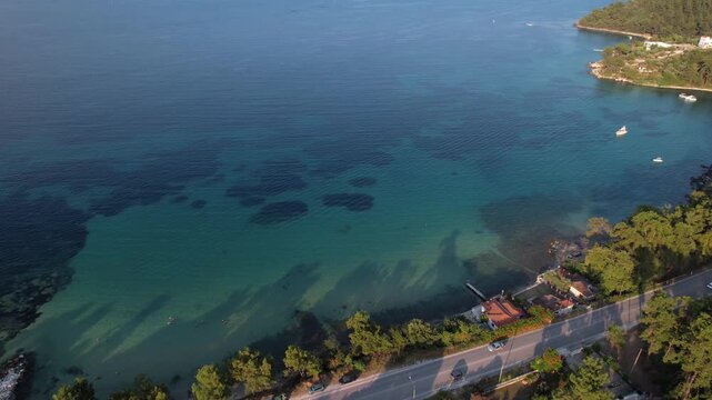 Beautiful aerial view of a sandy beach with crystal clear sea, turquoise water and visitors enjoying swimming and paddleboarding on Thassos Island, Greece.