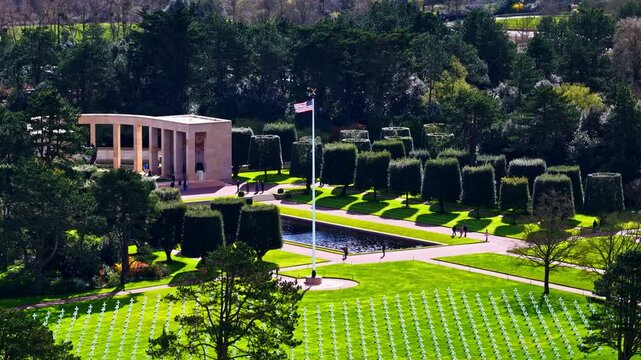 Aerial view of the Normandy American Cemetery and Memorial with rows of white crosses, manicured trees, and a reflecting pool in Colleville-sur-Mer, France.