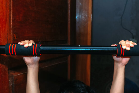 A front view of a person's hands gripping a black pull-up bar mounted on a wooden door frame.