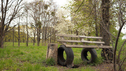 Handmade park bench made of timber and black tires on green glade in springtime. JPG © BorysiukN