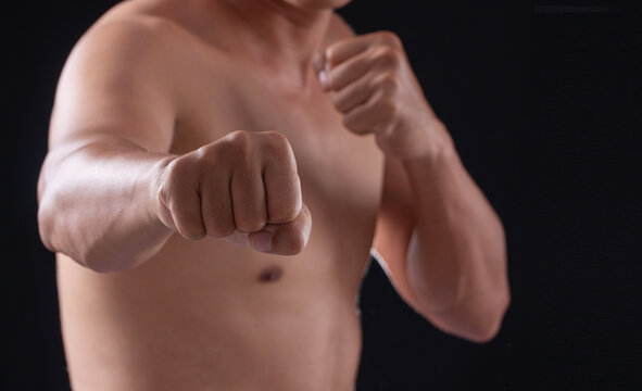 Close up of shirtless muscular man throwing punch to camera on dark black background with copy space. Aggressive male fighter training boxing or martial arts. Fitness power concept.