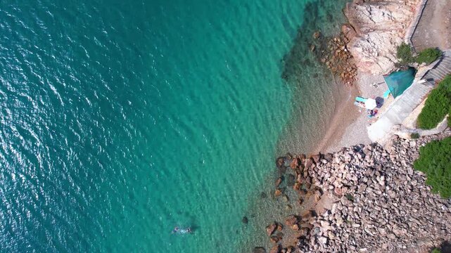 Beautiful aerial view of a sandy beach with crystal clear sea, turquoise water and visitors enjoying swimming and paddleboarding on Thassos Island, Greece.