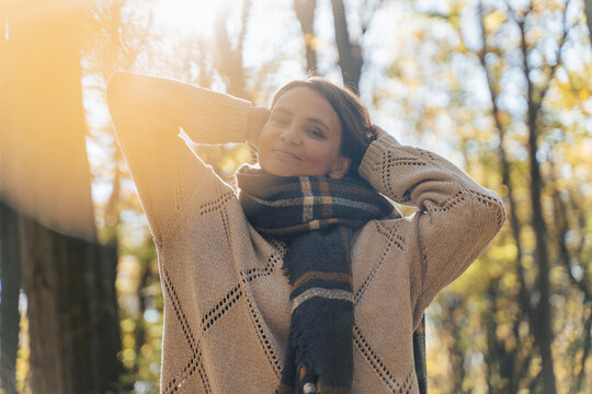 Mature Caucasian woman in warm sweater and scarf enjoying fresh air in autumn forest. Mental health and healthy aging concept