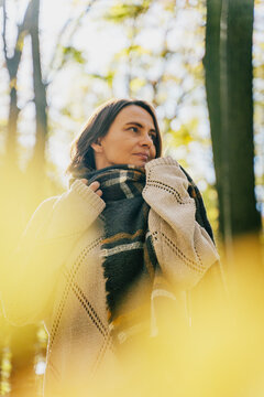 Mature Caucasian woman in warm sweater and scarf enjoying fresh air in autumn forest. Mental health and healthy aging concept