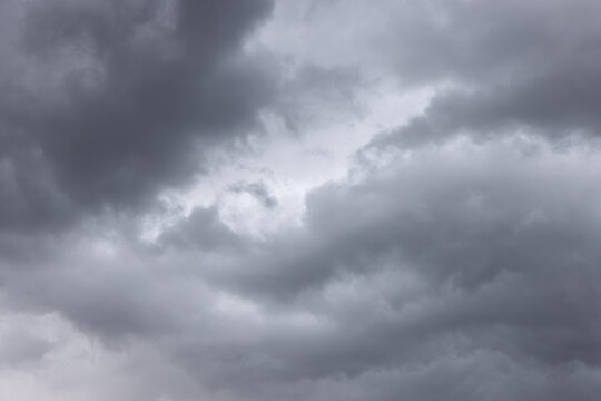 Rolling charcoal rain clouds surround a luminous break in the overcast sky, forming a textured full-frame study of unsettled weather.