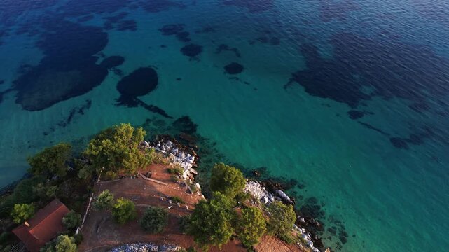 Drone aerial of a Aliki Beach secluded Mediterranean bay on Thassos, Greece with clear blue water, sandy shore, paddleboards, swimmers and stunning natural scenery.