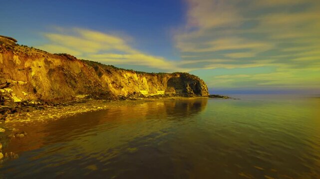 Dramatic cliffs and glowing sea at dawn, jagged outcrops casting silhouettes over tideswept shore, warm light carving textures into limestone faces, dynamic
