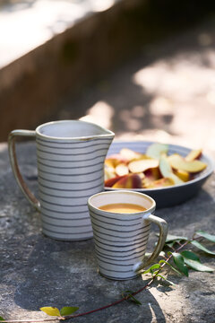 Close vertical view of sliced peaches and apples served in a striped ceramic dish with a cup of orange juice on a rustic outdoor stone table.