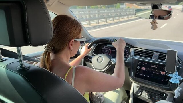 Woman driving car, holding keychain and gesturing while steering on highway. Interior point of view shot.