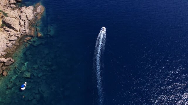 Aerial view of a fast motor yacht cutting through crystal-clear blue water. Vibrant textures, dynamic waves, powerful motion create the perfect visual for themes of luxury, freedom, vacation.