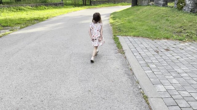 Cute toddler girl turning around while walking outdoors on a sunny summer day, follow-me tracking shot