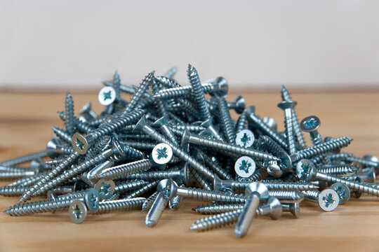 A pile of cross head wood screws on a pine board with white copy space behind