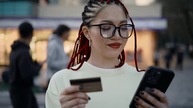 Young woman with red dreadlocks making mobile payment outdoors in city