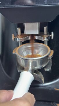 Coffee preparation, espresso grounds falling into a metal portafilter basket. Close-up macro shot showing professional barista workflow at a cafe station.