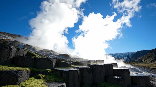 unique hexagonal basalt columns with green moss under blue sky and white clouds, geothermal steam rising from mountainside