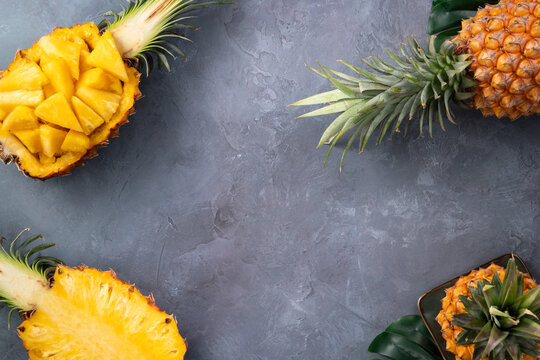 Fresh sliced pineapple fruits with green leaves on wooden board over dark gray textured background.