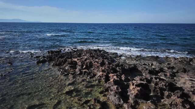 Volcanic rocks washed by clean sea waves, clear water and sharp rock formations on the shore of the Mediterranean Sea in Chania, Greece