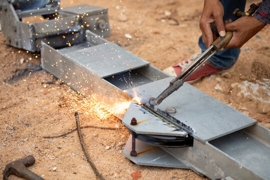 Worker cutting metal with torch without protective gloves showing safety violation on jobsite