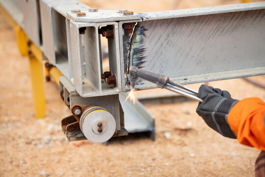 Worker disassembling complex metal structure using cutting torch at workshop