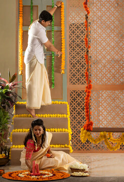 South Indian couple decorating house with flower garland to celebrate Onam
