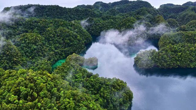 Aerial view of a tropical lagoon surrounded by lush green forested islands with mist rising from the turquoise and deep blue water in the Philippines.