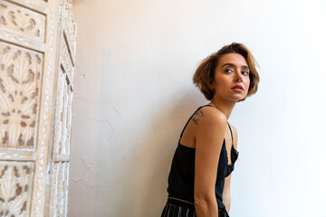 Fototapeta premium Woman with short hair in a black dress against a white wall.