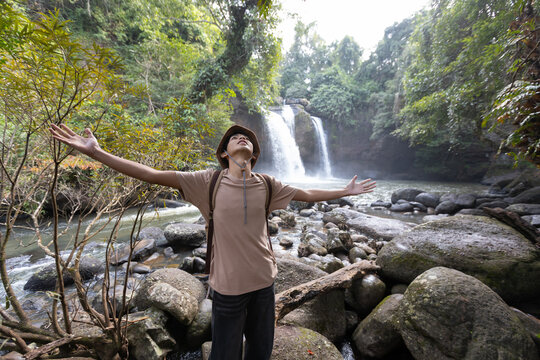 Asian Teenage Boy Standing with Outstretched Arms at Waterfall