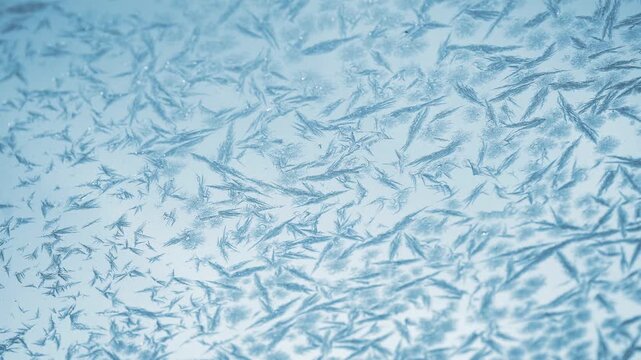 Macro view of delicate frost and ice crystal patterns spreading across a cold blue glass surface with subtle shimmering texture and abstract winter detail