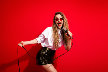 Obraz na płótnie Canvas Stylish woman in white shirt singing into microphone against red background exuding joy and energy