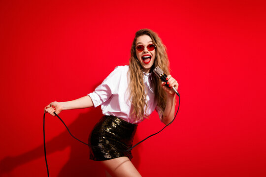 Stylish woman in white shirt singing into microphone against red background exuding joy and energy