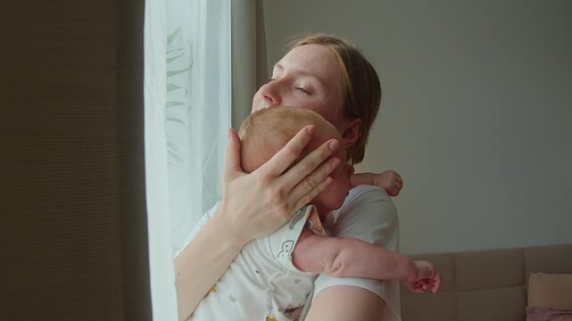Window light frames mother holding newborn with protective tenderness. Her posture and close embrace place child at center of scene, expressing safety, warmth, and dependable maternal care.