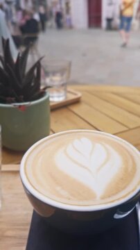 Vertical close-up of fern leaf latte art on a freshly made cappuccino at a bustling street caf&eacute; in Bratislava, capturing European caf&eacute; culture, travel, and relaxed city living.