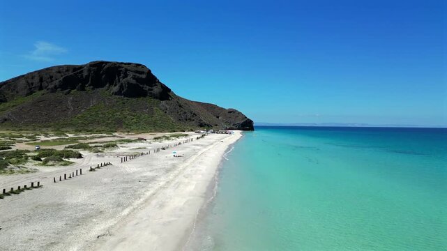 Drone pulls away over the waterline at El Tecolote Beach outside La Paz, facing Punta Shiro and revealing more of the shoreline as the camera retreats.