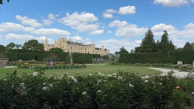 Formal gardens with blooming roses frame the Neo Gothic Lednice Castle in the Czech Republic beneath a bright summer sky. Historic architecture, cultural heritage, sightseeing and European travel dest