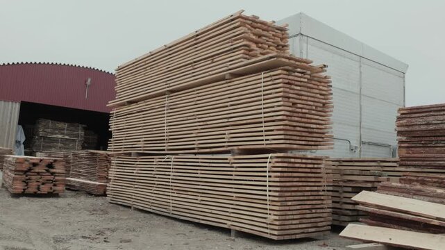 Wide view of bundled lumber boards stacked for drying and storage outside an industrial sawmill facility under an overcast sky