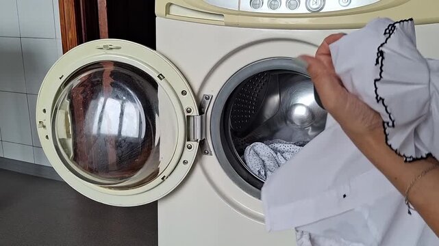 Washing clothes in a washing machine at home, in the kitchen, on a sunny day.
