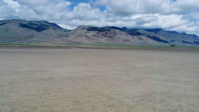 A cinematic drone racing backward low over the Alvord Desert salt flats, revealing vast cracked playa and Steens Mountain on the horizon in remote southeastern Oregon.