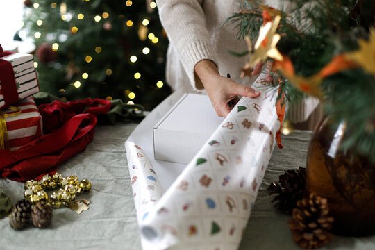 Female hands in knitted sweater cutting paper with vintage scissors while wrapping presents. Cozy Christmas eve atmosphere, handmade gift preparation, scandinavian interior decoration