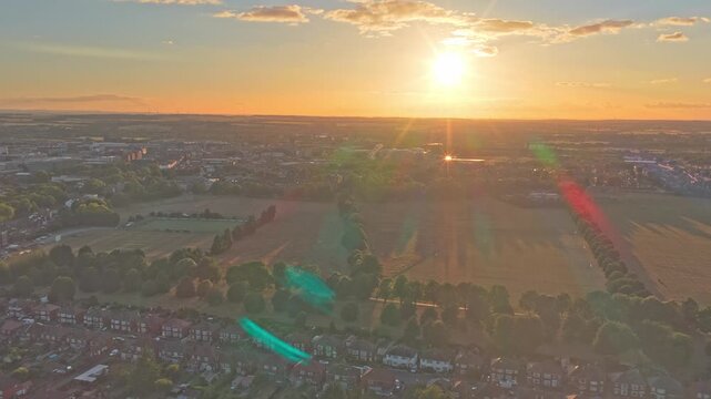 Residential neighborhoods and expansive green parkland in Doncaster, South Yorkshire, England, glow beneath low golden sunlight with long shadows and lens flare, drone forward flyover.