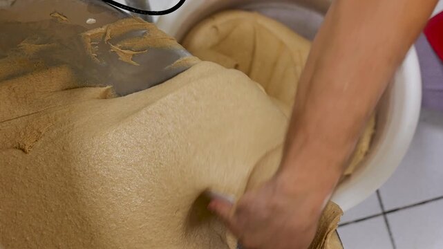 A baker's hand guides soft dough into a proofing bucket, shot from a low angle.