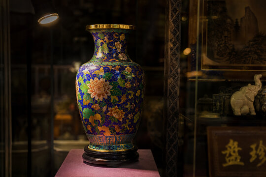 Antique shop window display featuring a cloisonne vase under a spotlight.