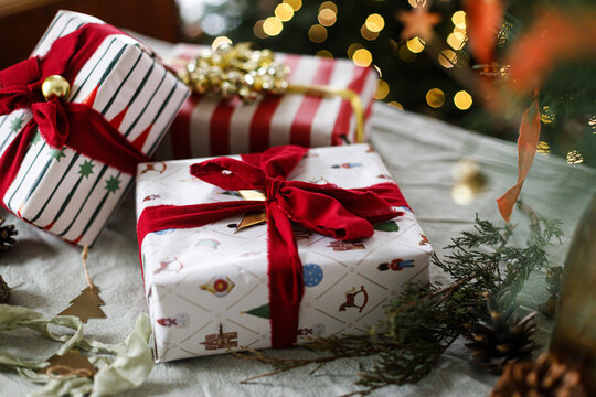 Merry Christmas! Stylish wrapped Christmas gift boxes on table on background with decorated xmas tree and warm glowing bokeh lights. Cozy winter holiday celebration, xmas eve atmosphere