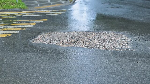pothole on a city street that is filled with rainwater. Water collects in the pothole, creating a hazard for drivers and pedestrians in the area